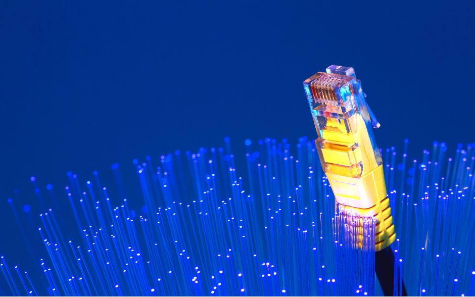 Yellow fiber network cable stands out amidst a backdrop of blue illuminated optic fibers, set against a dark blue background